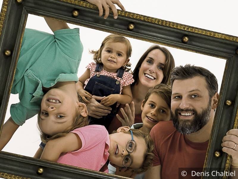 Photo de famille avec 4 enfants et 2 parents, ils tiennent un cadre et sourient.